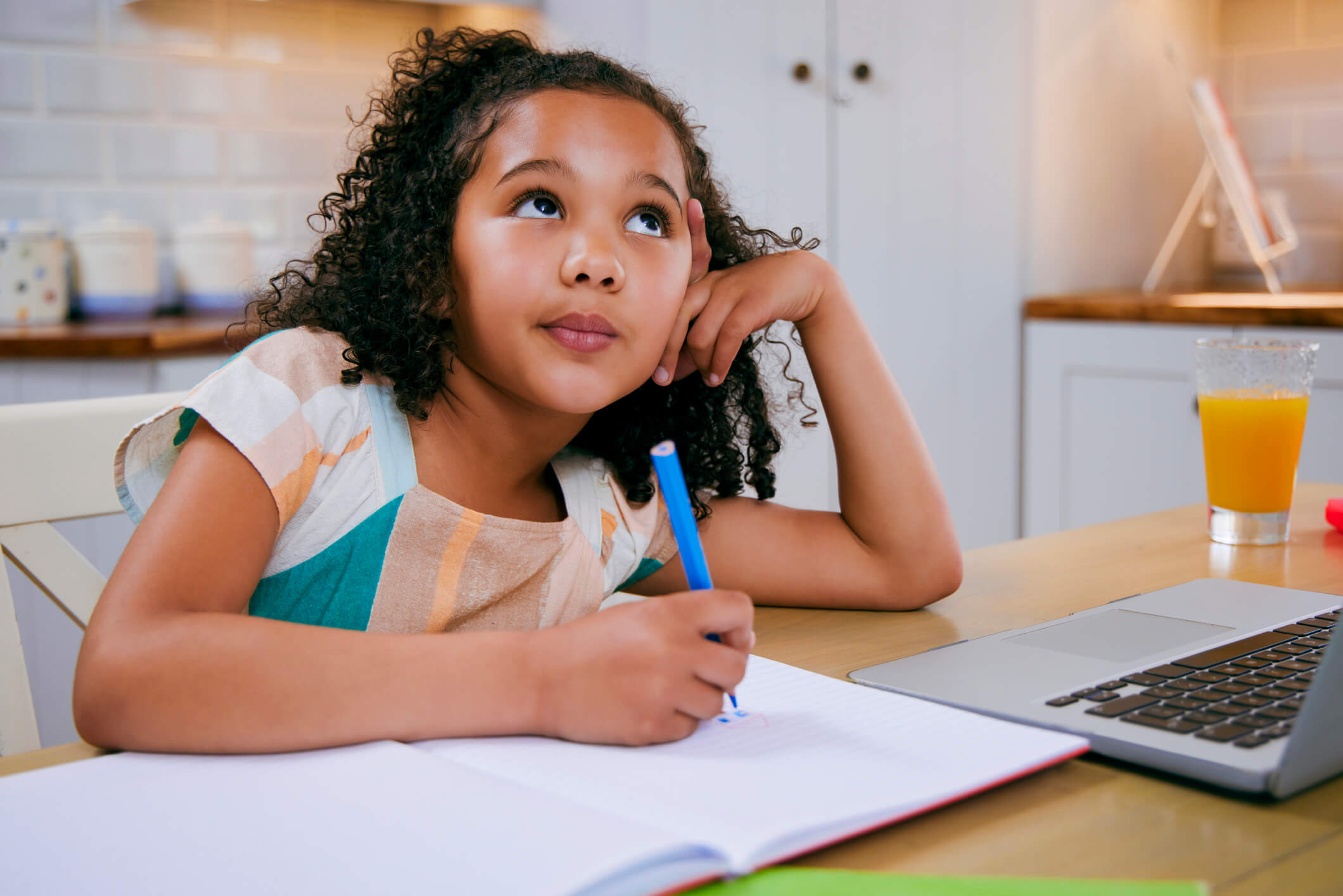 Young girl thinking while writing in her notebook.