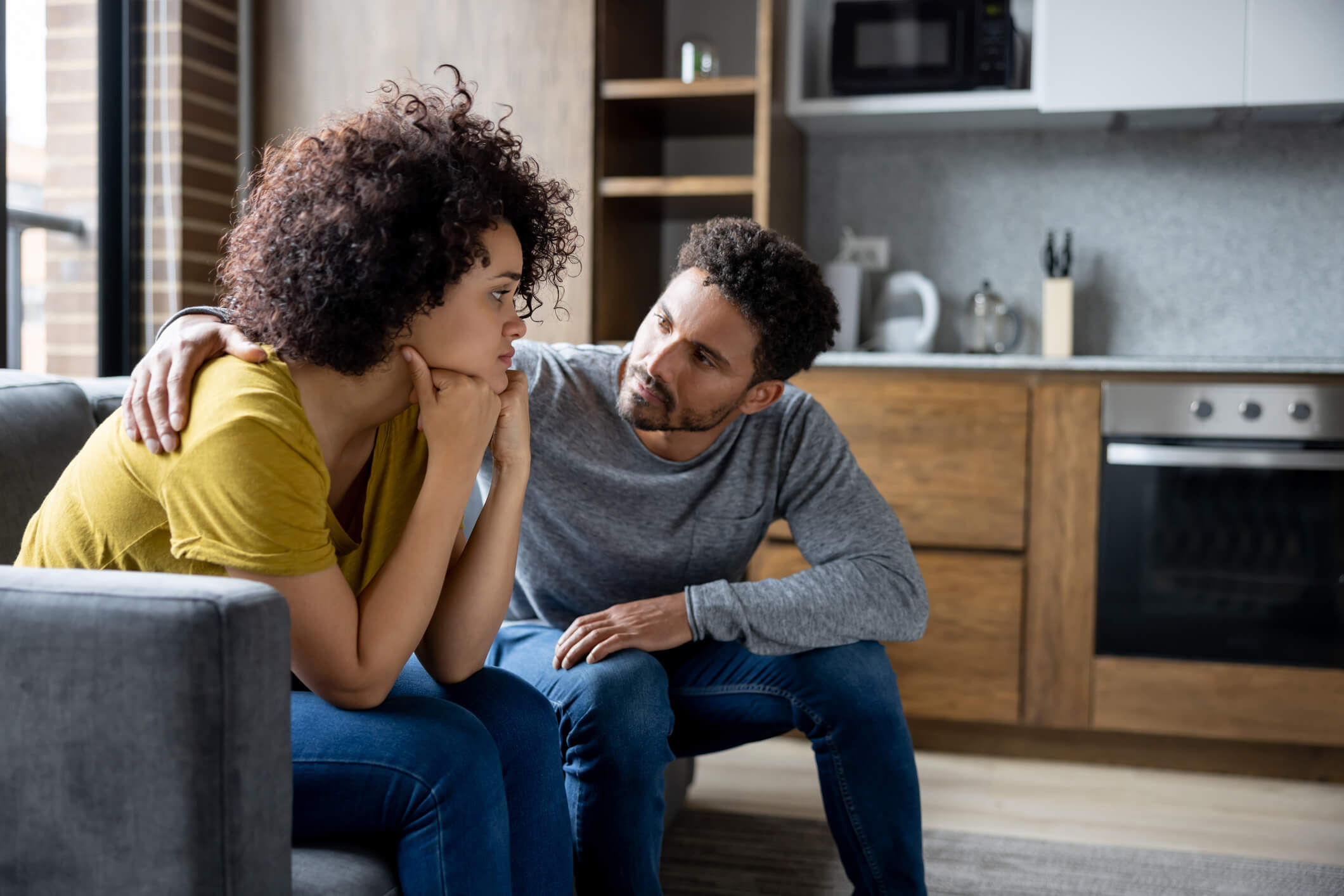 Man sitting on a couch consoling a distressed young woman.