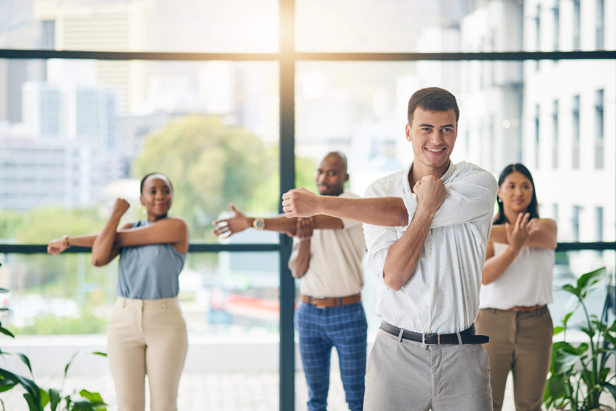 Health coach leading a group of individuals in an arm over chest stretching exercise.