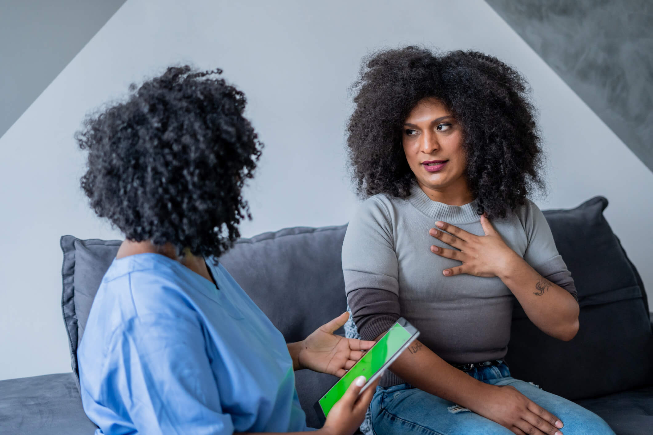 Woman sitting on a couch with her hand to her heart talking to a healthcare provider across from her.