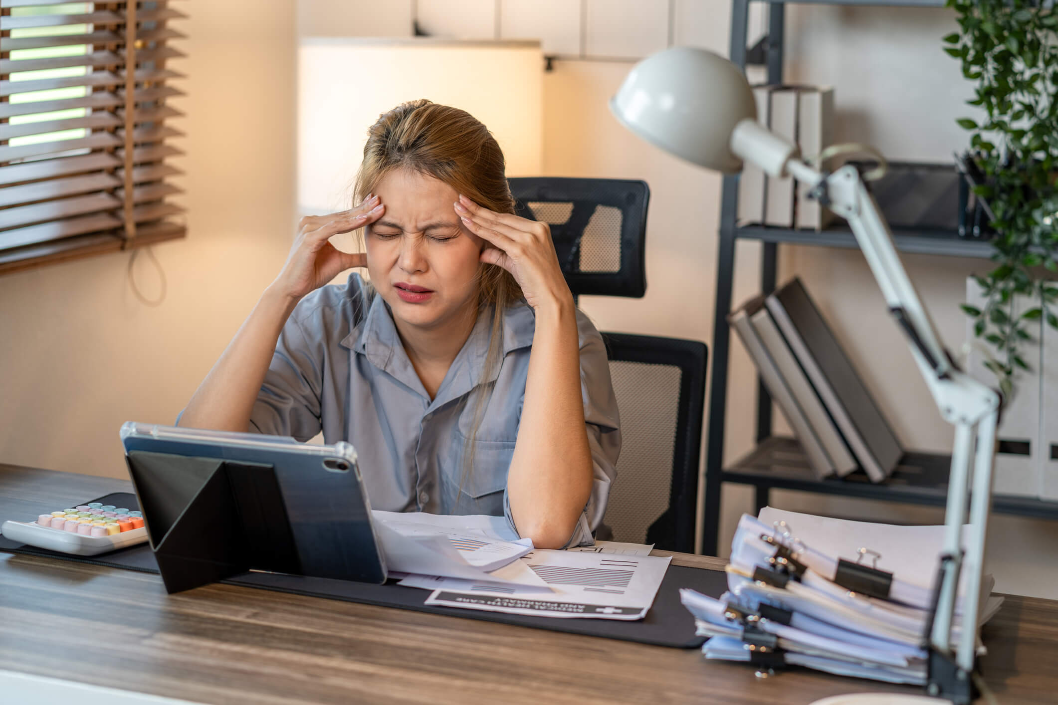 Woman with a distressed look on her face and her head in her hands sitting at a desk.