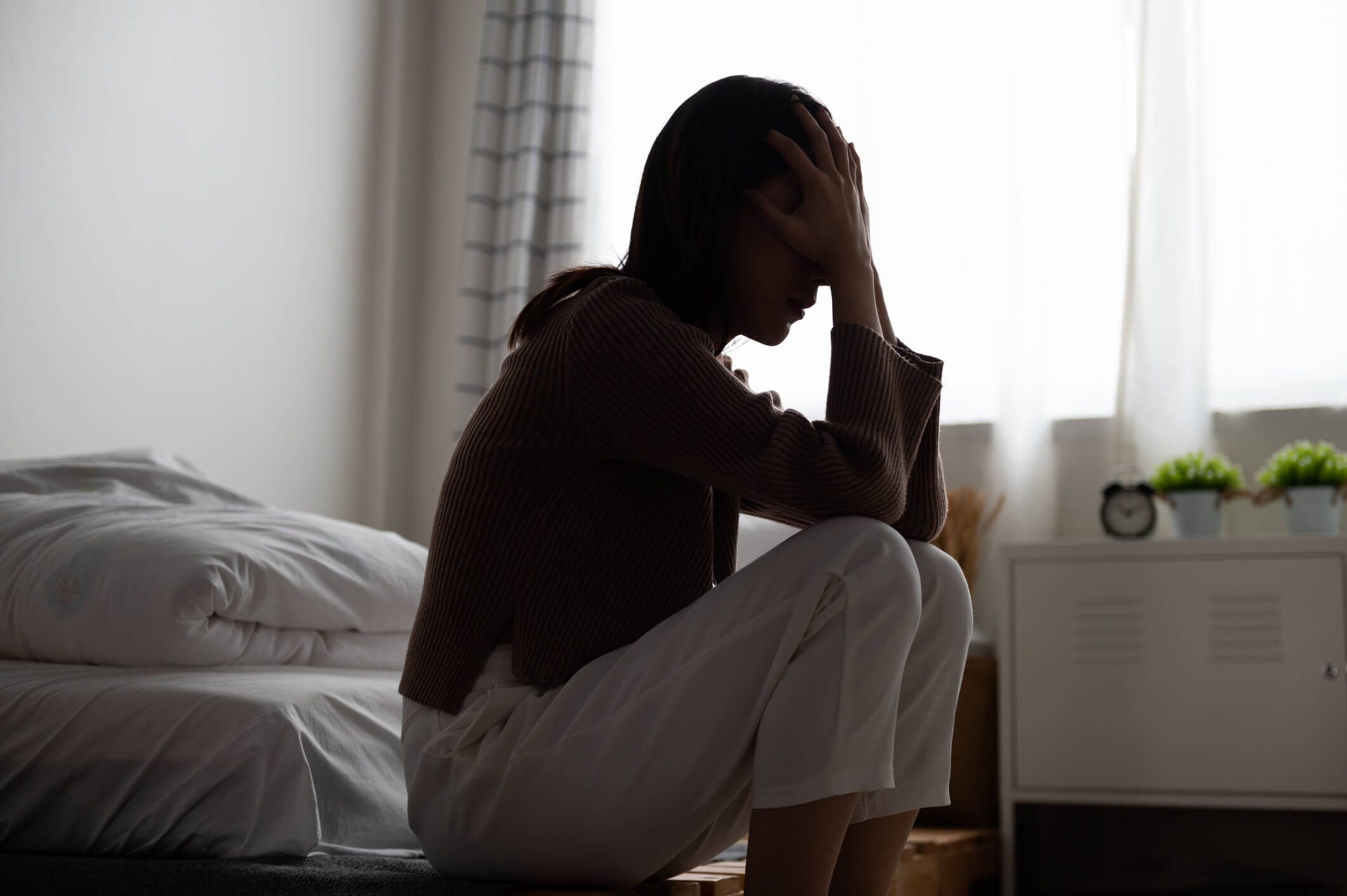 Shadow of a woman sitting on a bed with her head in her hands.