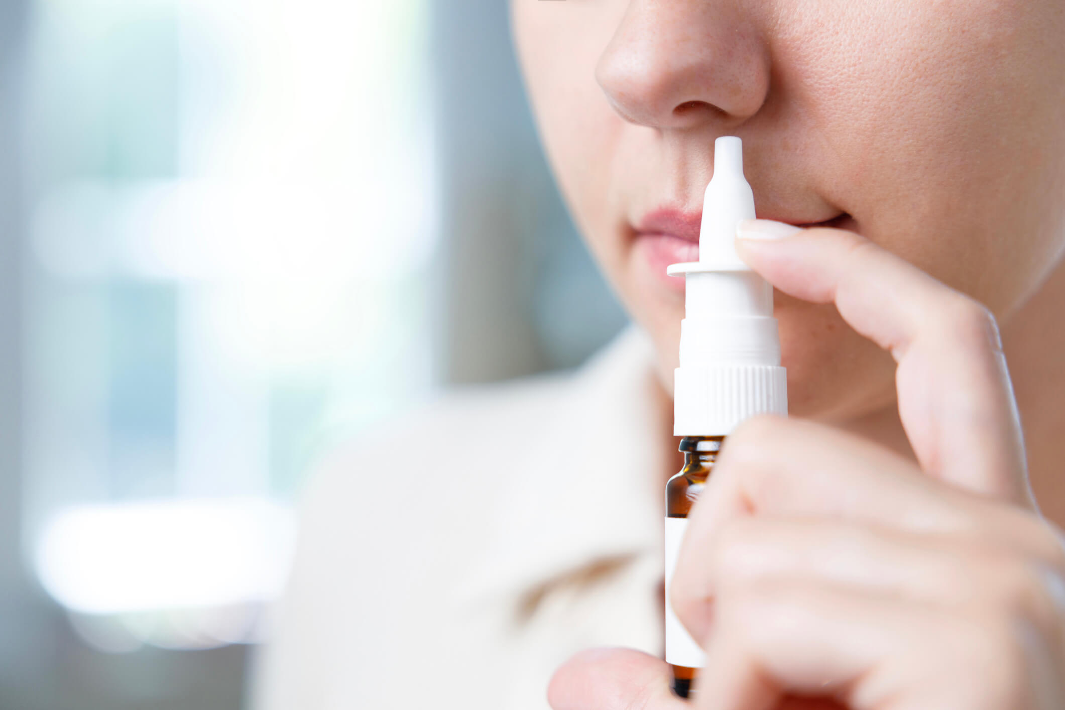 Woman holding nasal spray up to her nose.