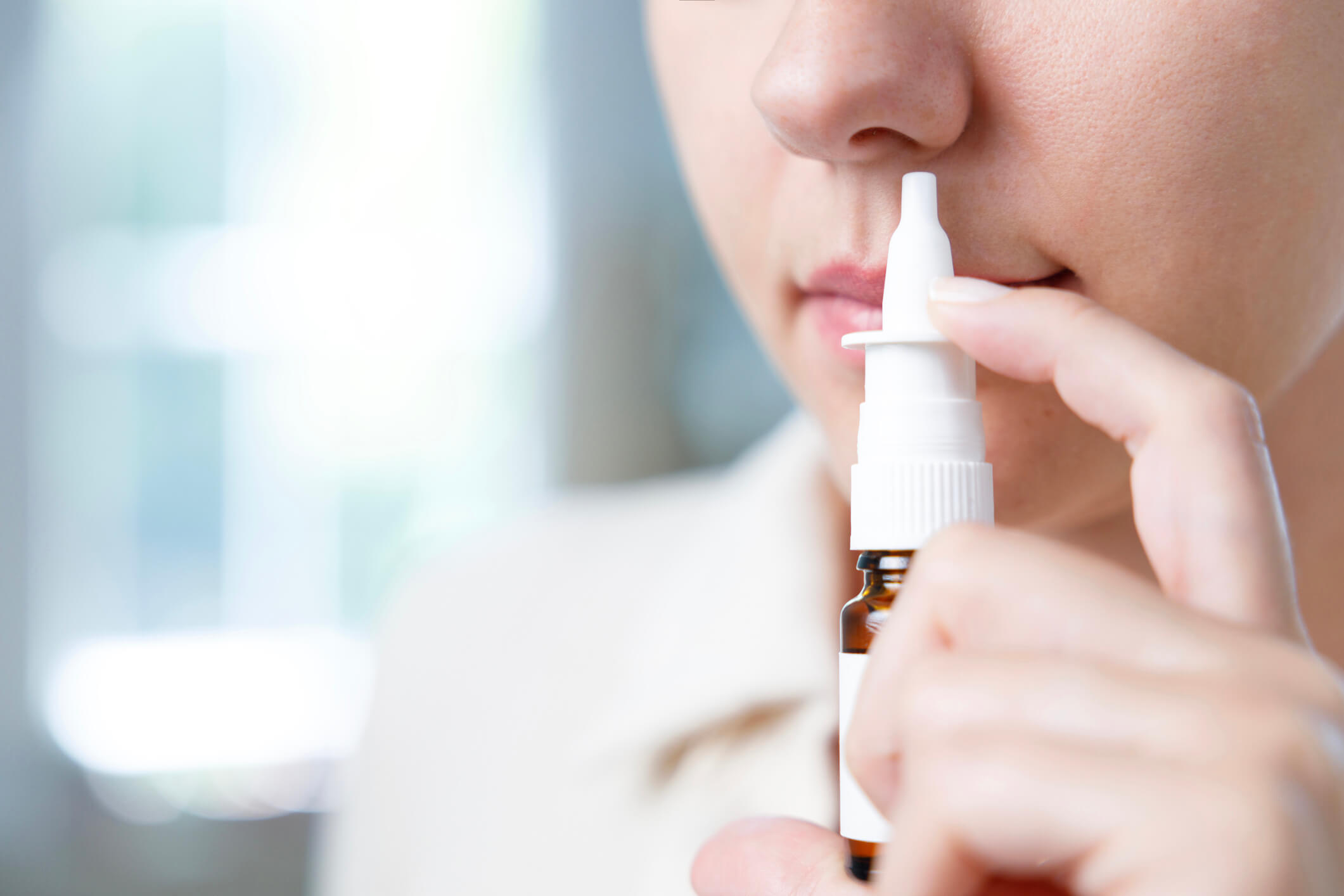 Patient holding up esketamine nasal spray to their nose to administer for treatment-resistant clinical depression.