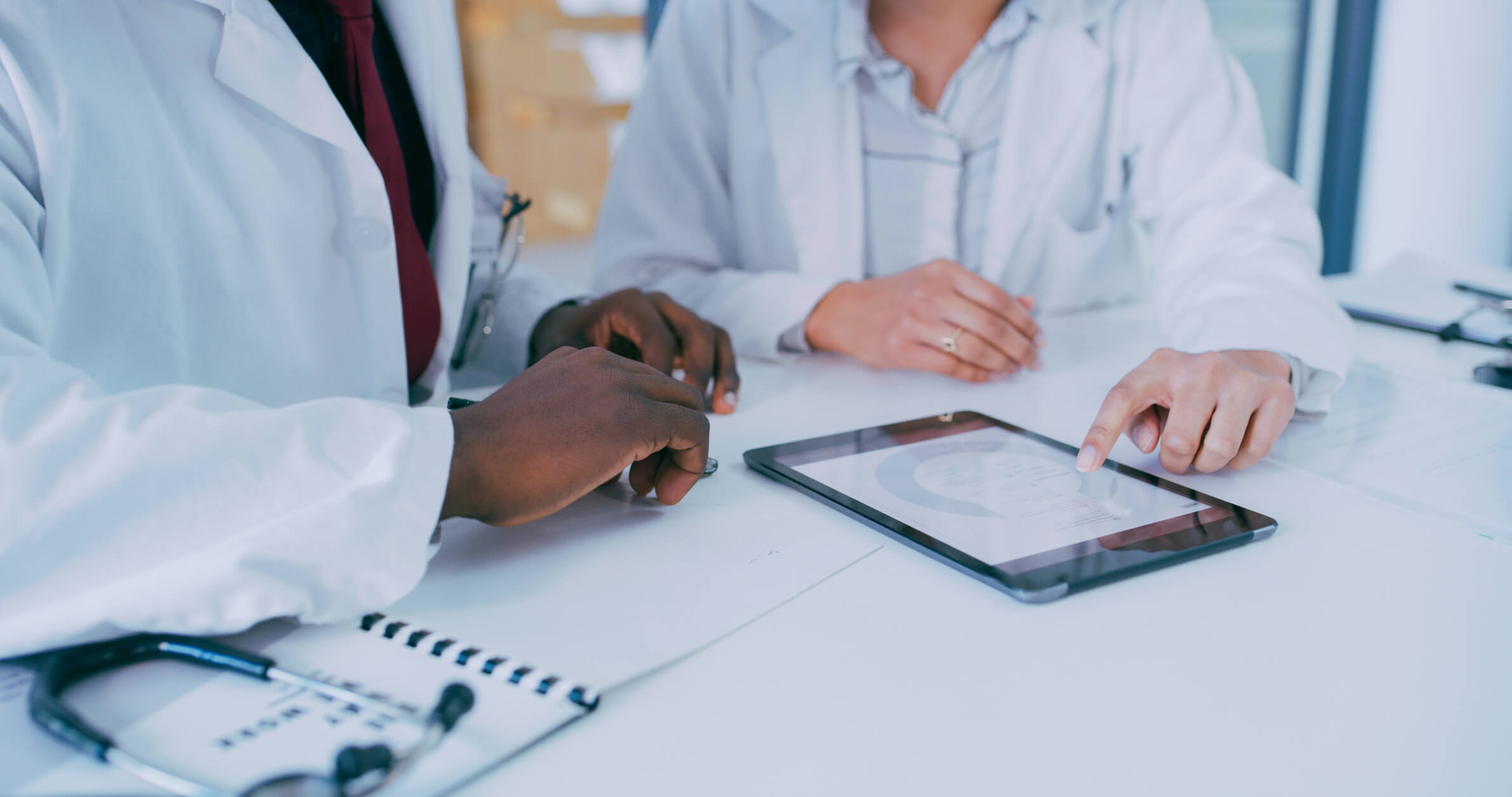 Tablet on a table with a doctor in a white coat pointing at the doctor referrals on the tablet screen.