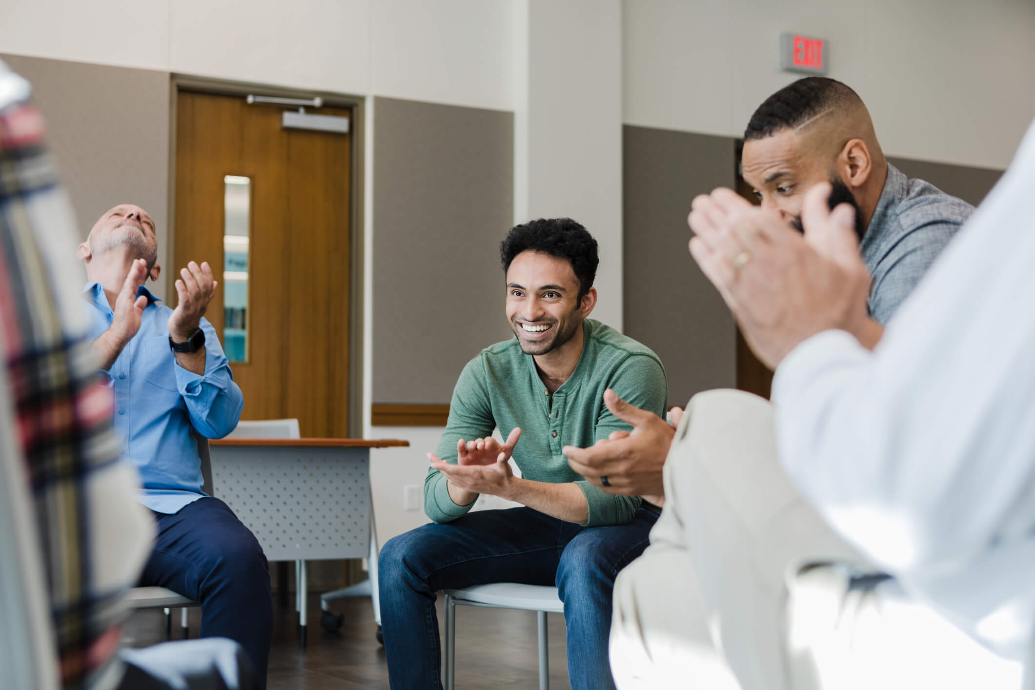 A man wearing a green shirt in a support group clapping along with the rest of the group sitting in chairs.