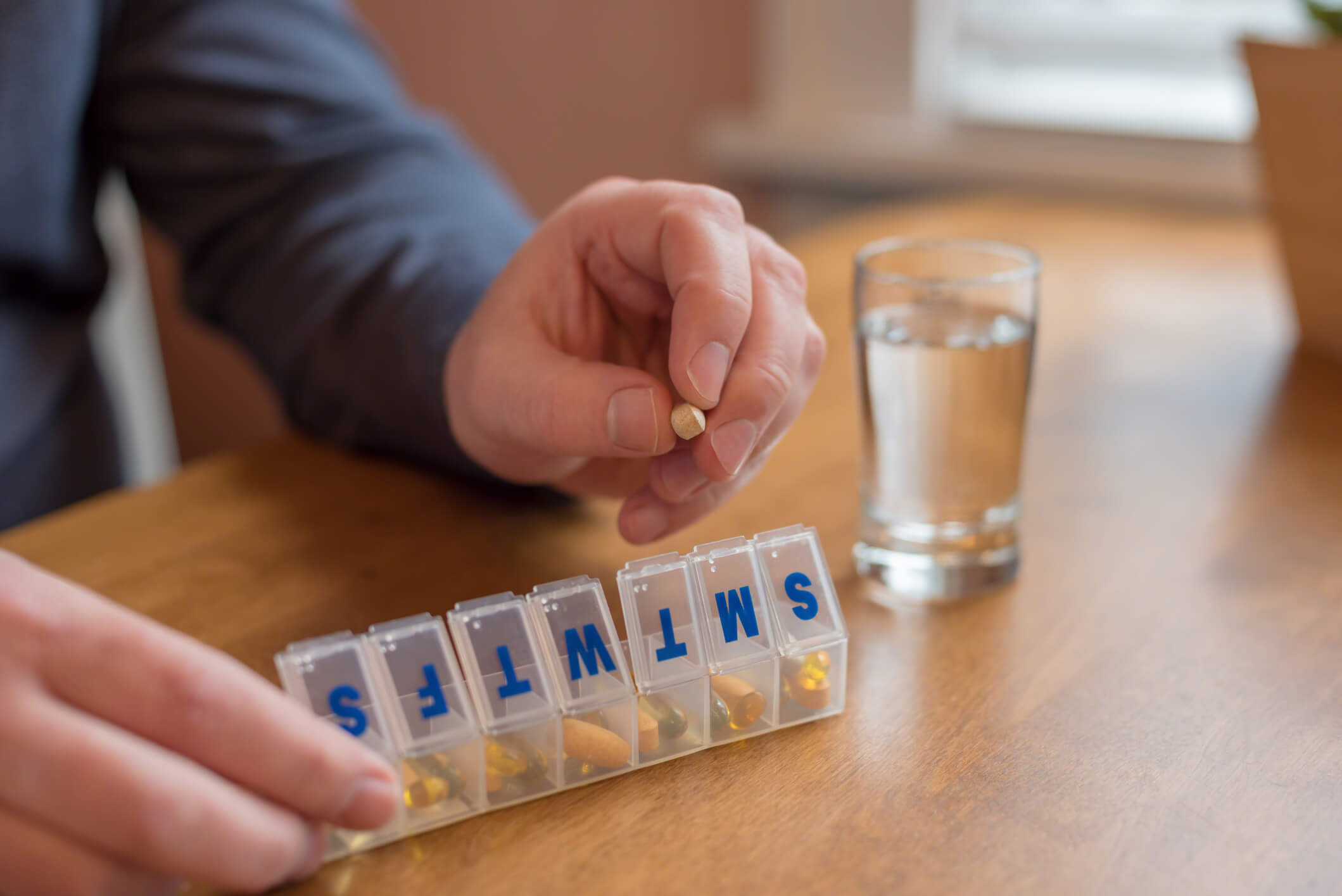 Patient engaging in medication management with a pill scheduler for the week. Each pill slot has the initial of the day of the week.