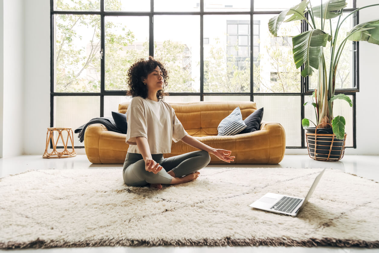 Woman meditating on a white rug at home.