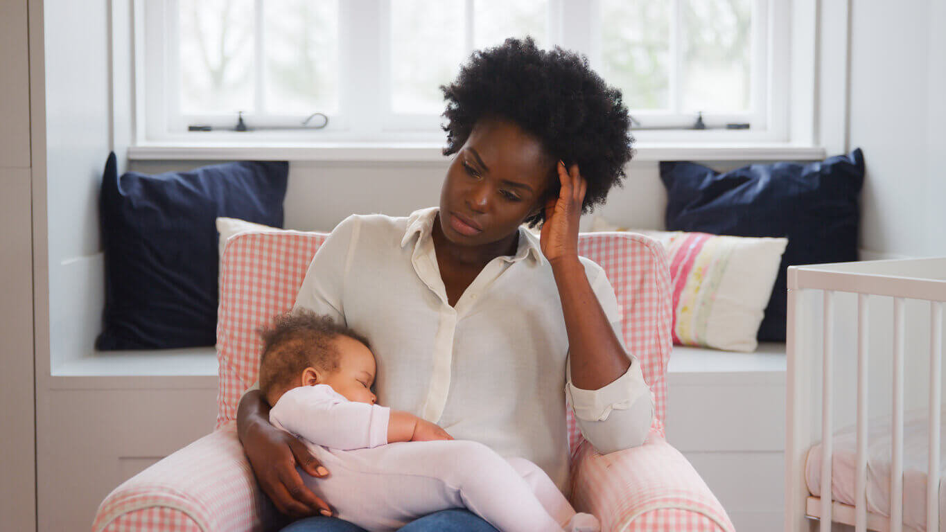 Image of a new mother experiencing postpartum depression while holding her sleeping baby daughter in a nursery at home.