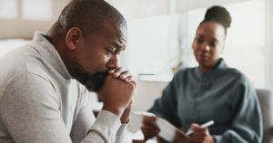 A therapist is speaking in the office with a male patient, discussing mental health advice during anxiety therapy.