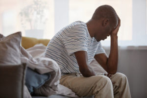 A black man sitting on bed in morning struggling with major depression.