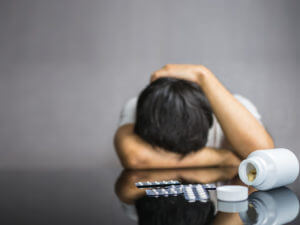 Antidepressants pills and medicines on table with depressed man facing down.